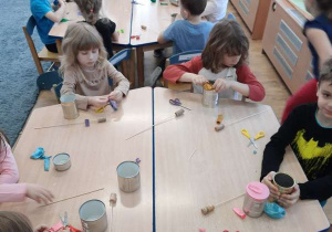 Dzieci siedzą w sali i wykonują bębenki z metalowych puszek i balonów.